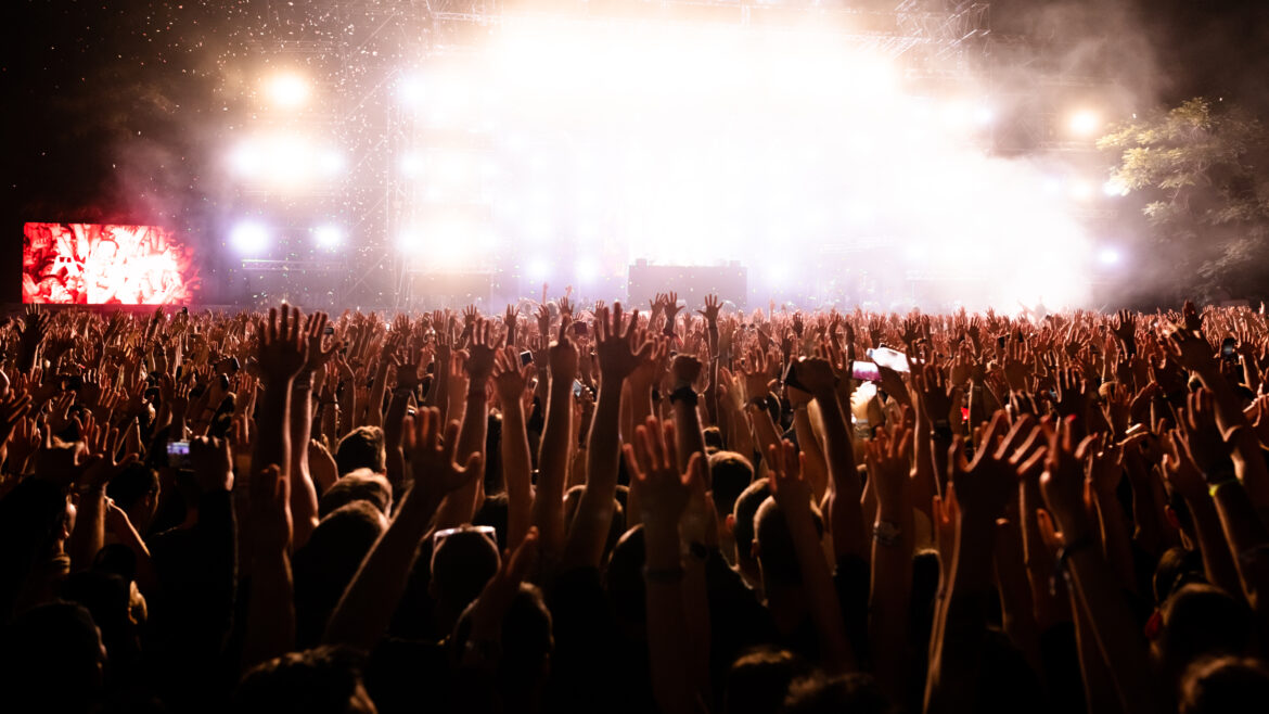 Crowd of fans with arms raised watching confetti fireworks at music concert.