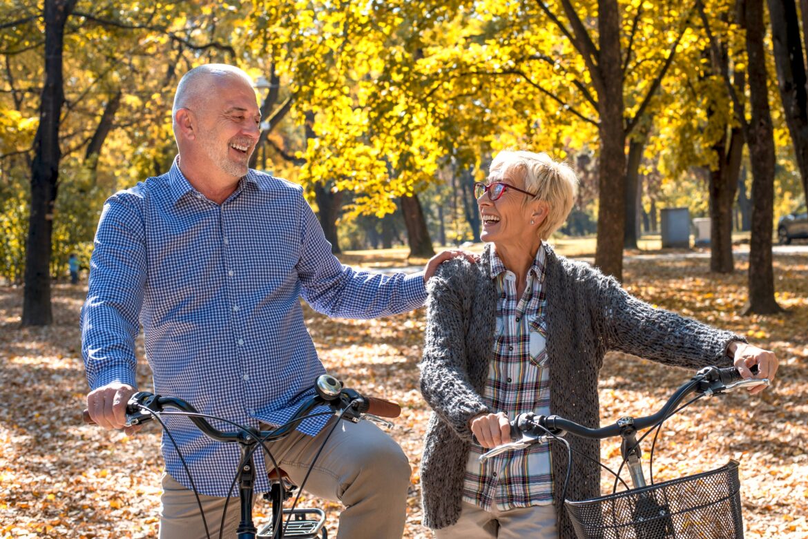 Happy elderly couple riding a bicycle in the park in the autumn